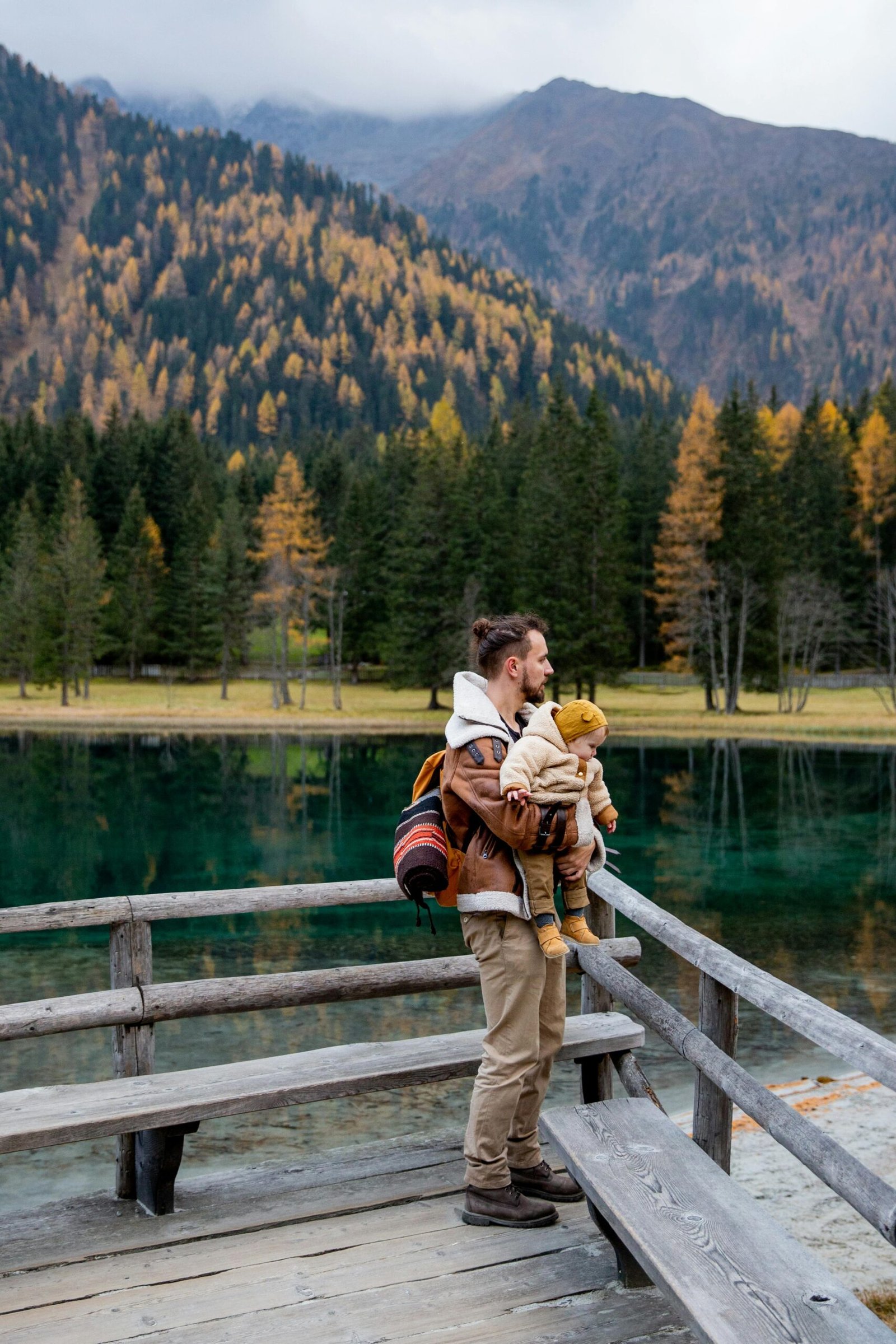 A father holds his toddler as they admire a beautiful mountain lake scenery.